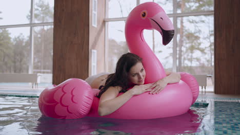 Eine-Entspannte-Frau-Genießt-Den-Tag-Im-Spa-Oder-Wellnesscenter-Und-Schwimmt-Auf-Einem-Rosa-Aufblasbaren-Flamingo-Im-Schwimmbad